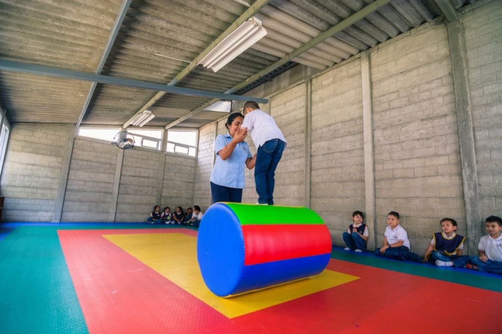 Maestra ayuda a un niño de preprimaria a hacer un ejercicio de equilibrio