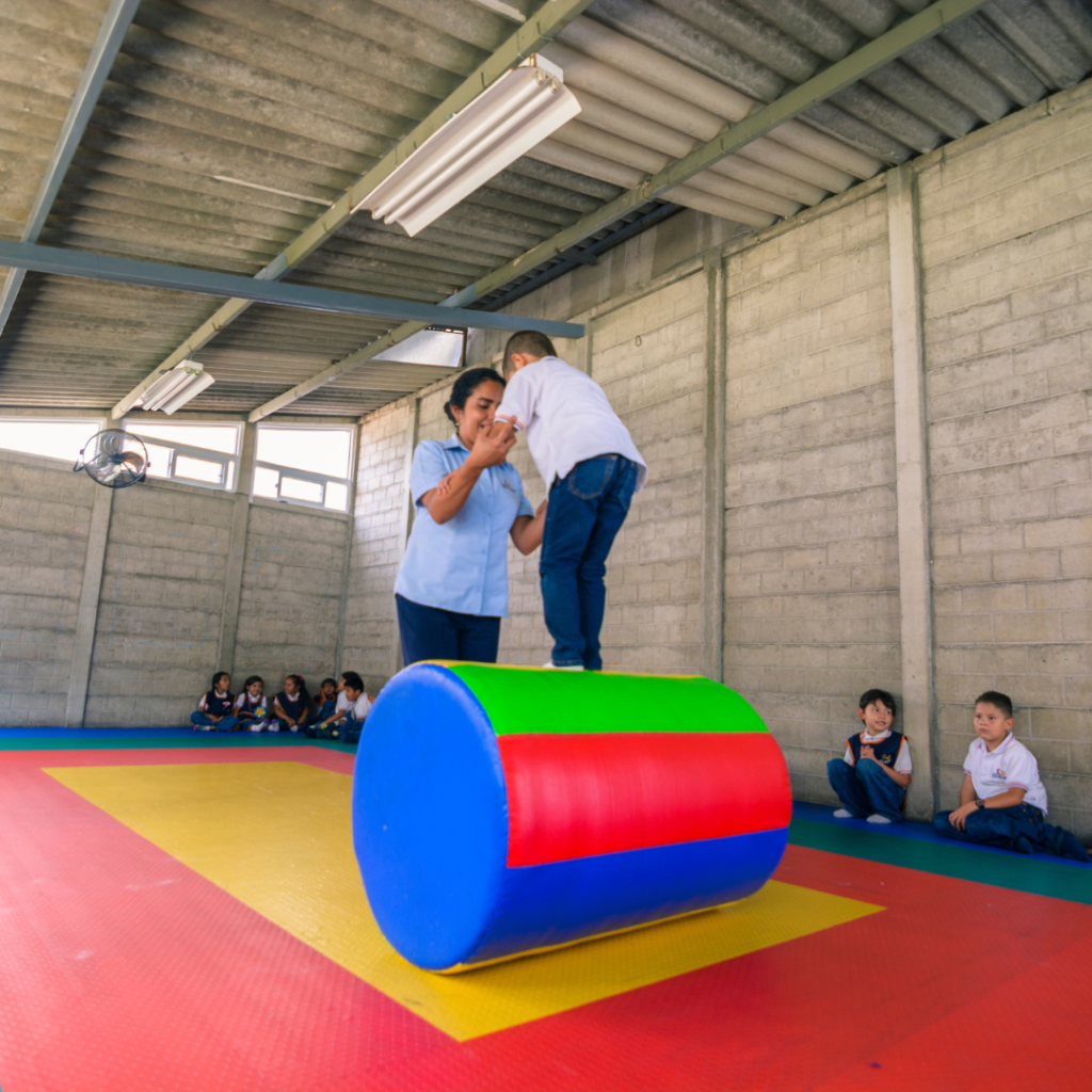 Un niño de 4 años sobre un cilindro acolchado guiado por su maestra.